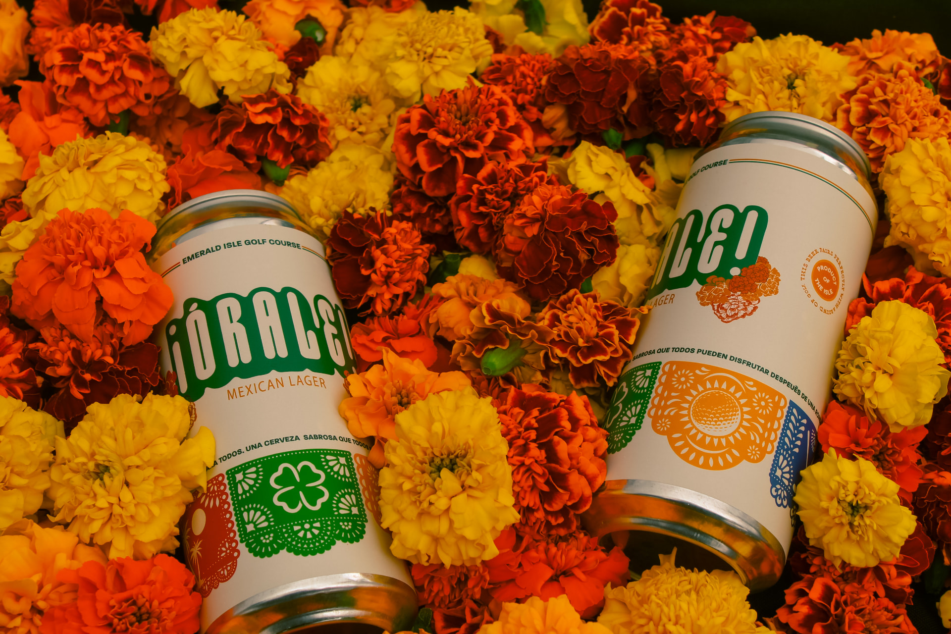 Cans of the official Órale Mexican lager resting in a bed of marigolds