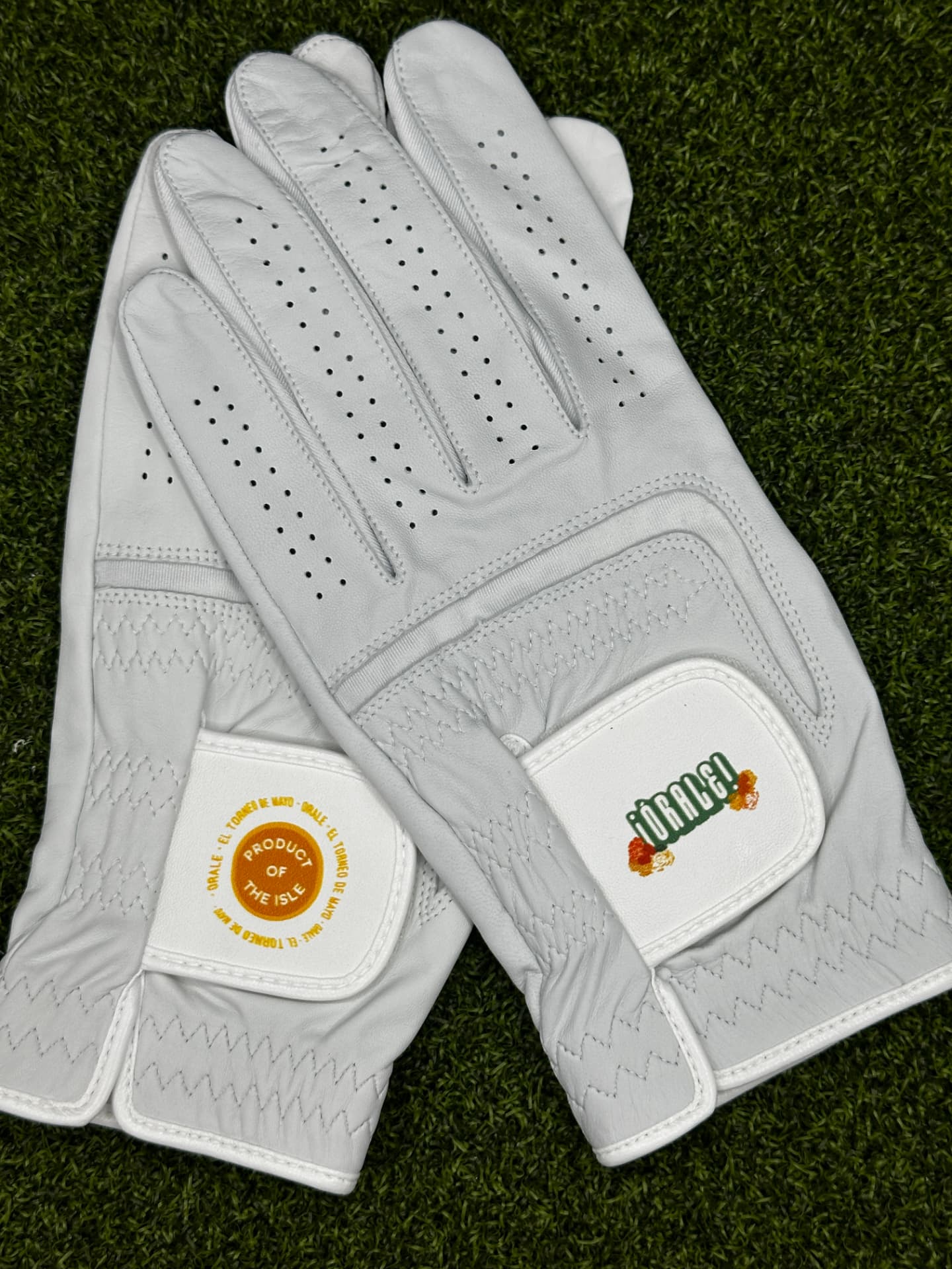 Pair of leather golf gloves with Órale tournament branding on the wrist flaps